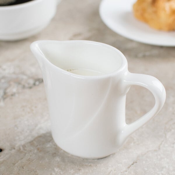 A white pitcher with a handle on a table.