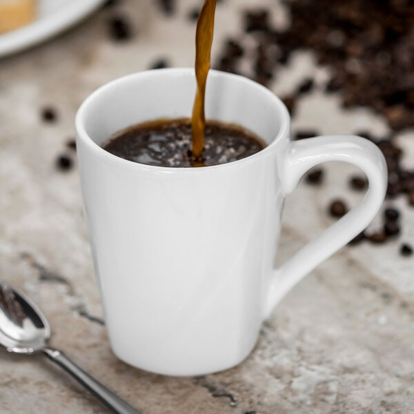 A spoon pouring coffee into a white Tuxton China mug.