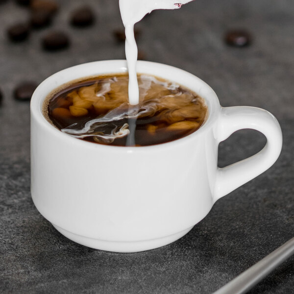 A Tuxton San Marino AlumaTux Pearl White espresso cup filled with brown liquid and milk.