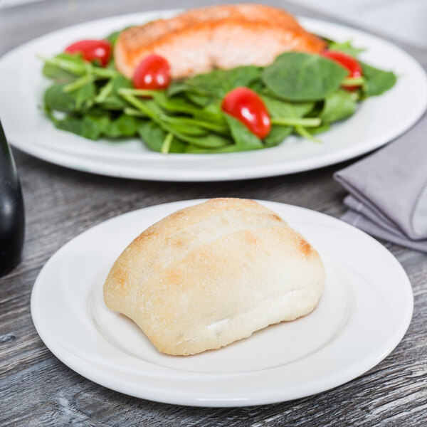 A Tuxton AlumaTux Pearl White china plate with a bread roll and salad on it.