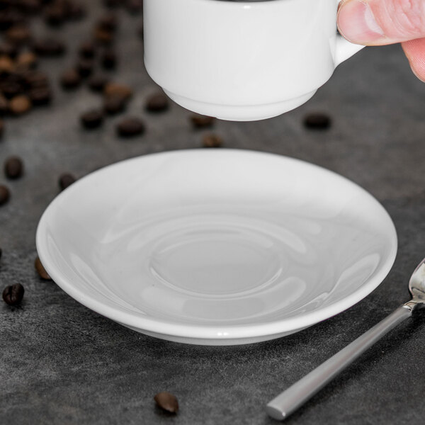 A hand holding a Tuxton Pearl White saucer under a white cup being poured into.