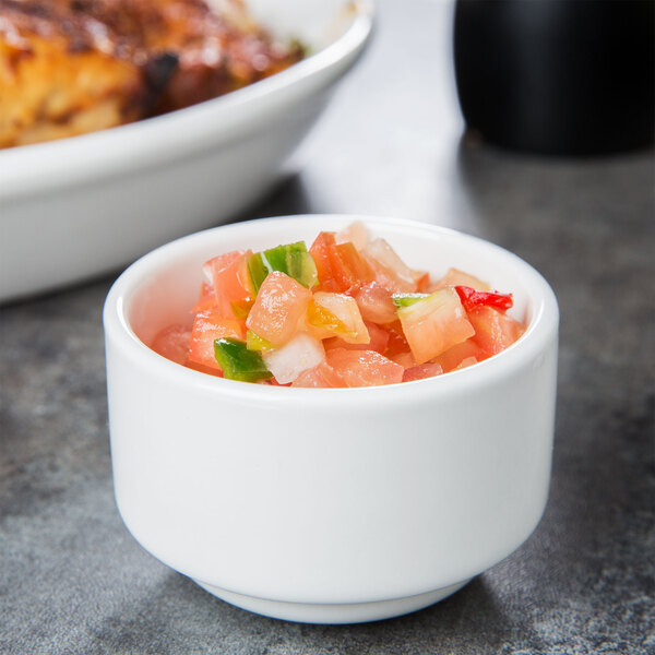 A stackable white Tuxton ramekin filled with salsa on a table.