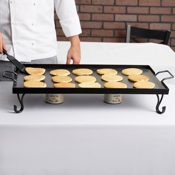 A chef cooking pancakes on an American Metalcraft wrought iron griddle on a stand.