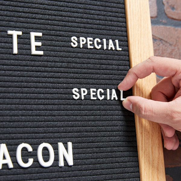 A person using an Aarco Helvetica letter and number set to touch a white plastic sign with the words "special bacon"