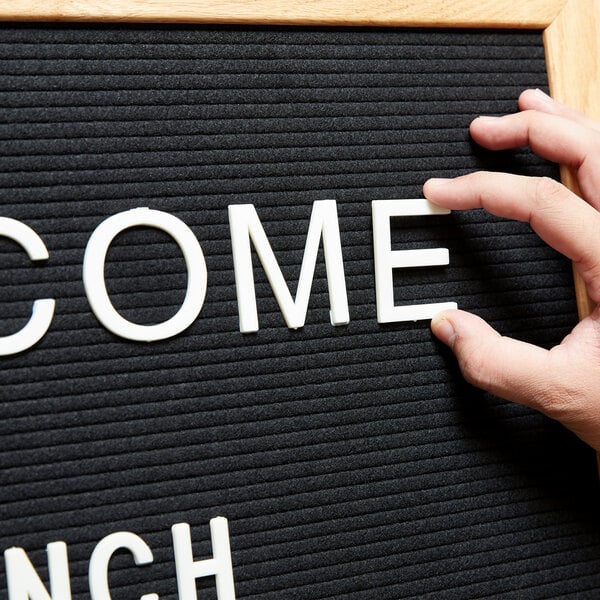 A person's hand using Aarco Helvetica letter and number set to change a letter board to say "Welcome Lunch"