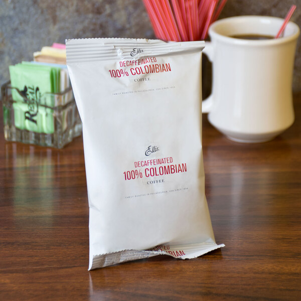 A white packet with red text that reads "Ellis 100% Colombian Decaf Coffee" sits on a table.