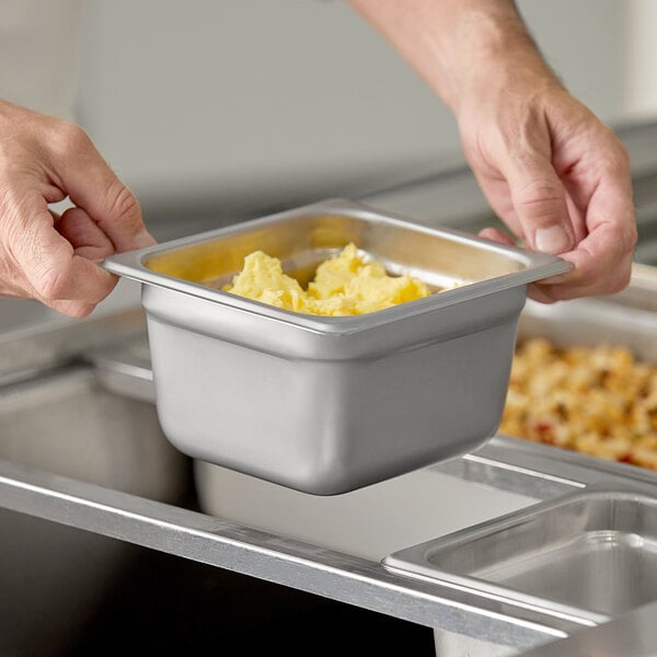 A person holding a Choice stainless steel steam table pan filled with food.