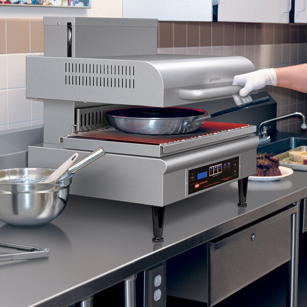 A woman using a Hatco countertop salamander to cook food in a professional kitchen.