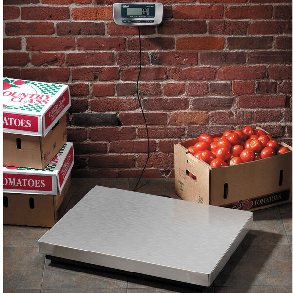 An Edlund digital receiving scale on a white surface with boxes of tomatoes on it.