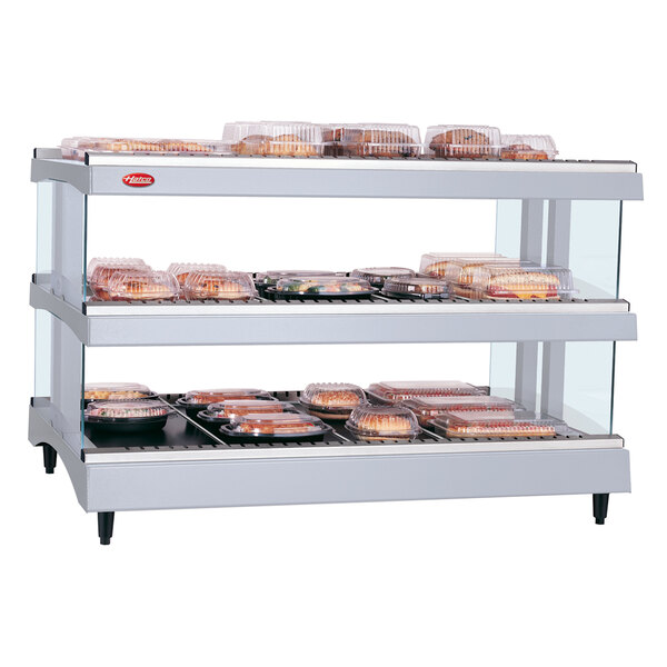 A Hatco white granite heated glass display shelf with trays of food.