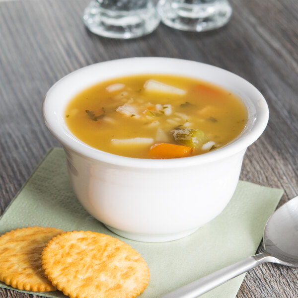 A white Fiesta china bouillon bowl filled with soup and crackers on a table.