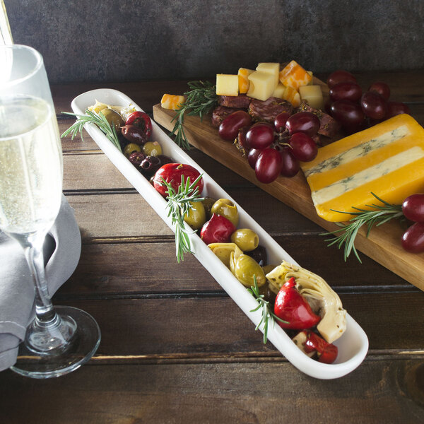 A white porcelain 10 Strawberry Street olive server on a table with a glass of wine, cheese, and fruit.