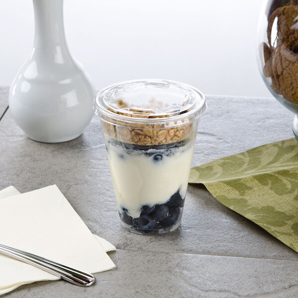 A narrow plastic parfait cup filled with yogurt and blueberries with a spoon.
