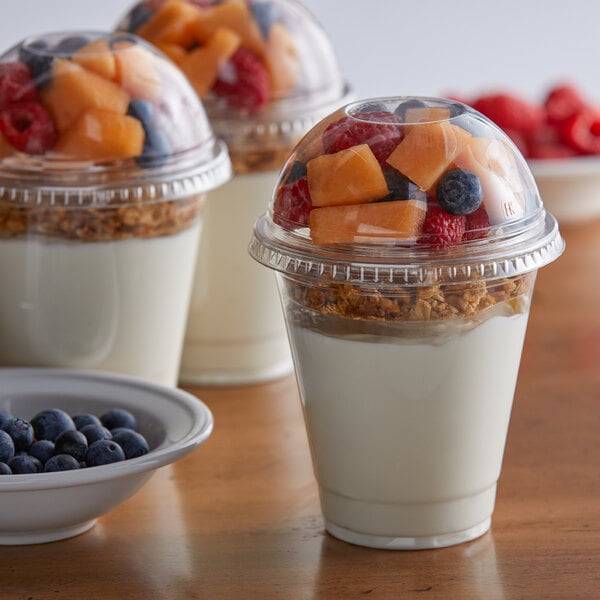 A group of 12 oz. plastic parfait cups with fruit and yogurt in them.
