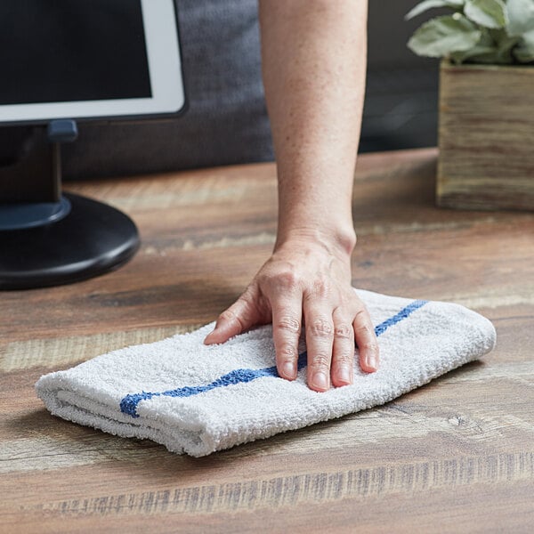 A hand using a blue and white striped Choice bar towel to clean a counter.