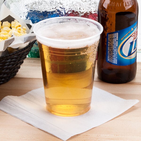A Solo Ultra Clear PET plastic cup filled with beer on a table with a glass of beer and a bottle of beer.