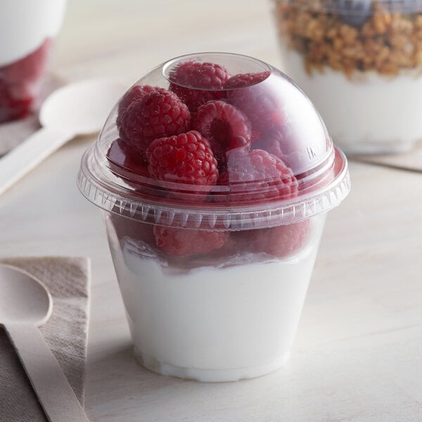 A Squat plastic parfait cup filled with yogurt, raspberries, and granola with a spoon on a napkin.