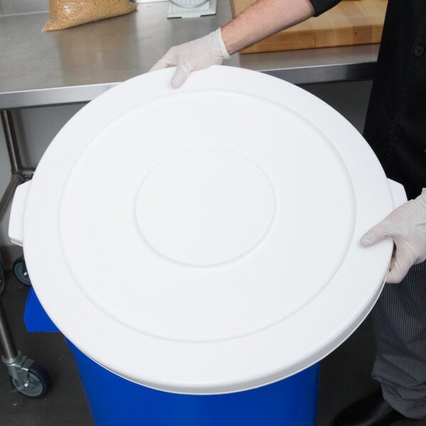A person in gloves holding a white lid for a Continental 44 gallon round trash can.