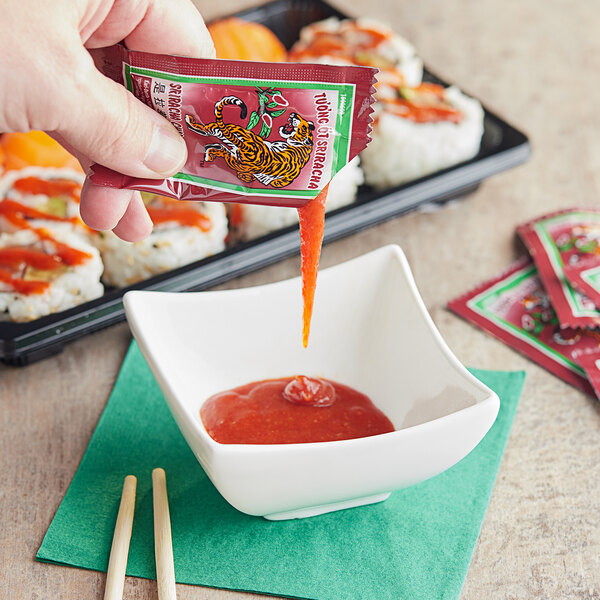 A hand pouring Sriracha sauce into a bowl of sauce.