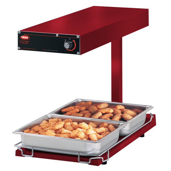 A red Hatco food warmer with trays of tater tots and chicken on a heated shelf.