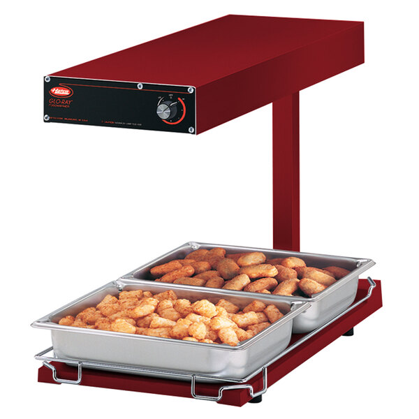 A red Hatco Glo-Ray food warmer with trays of tater tots and other food on it.