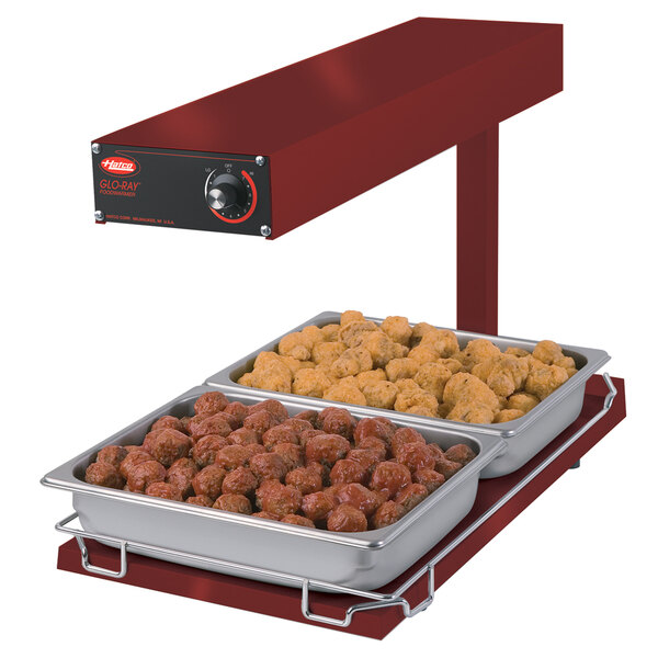 A red Hatco food warmer on a counter with trays of meatballs and chicken.