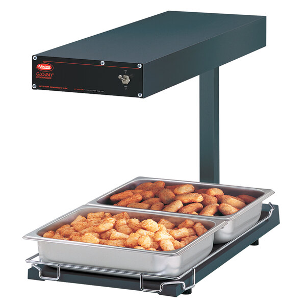 A Hatco heated food warmer on a counter with tater tots and trays of food.