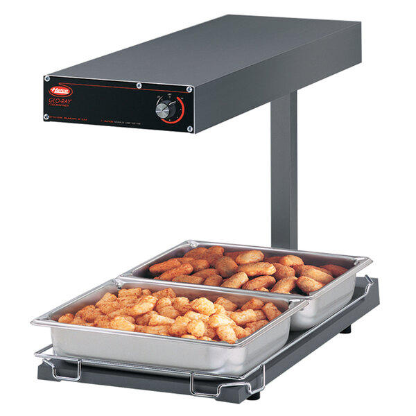A Hatco heated shelf food warmer on a counter with trays of tater tots inside.