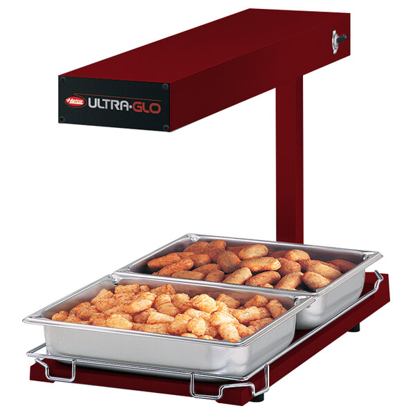 A red Hatco Ultra-Glo food warmer with two trays of food on a counter.
