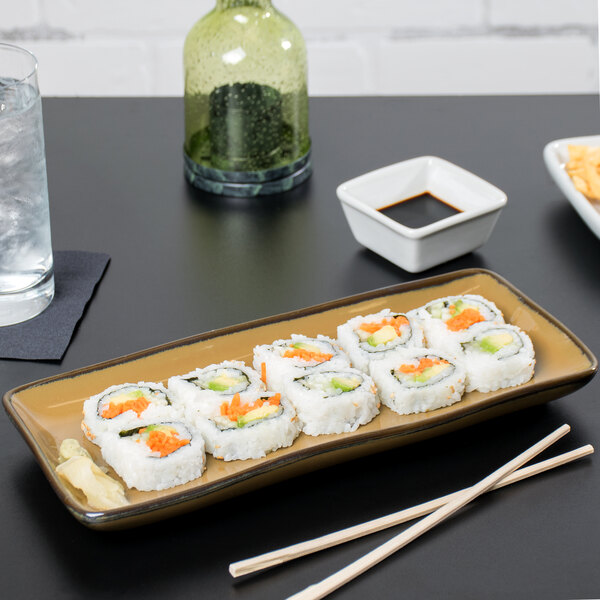 A Tuxton Mojave china tray holding a sushi roll with chopsticks on a table.