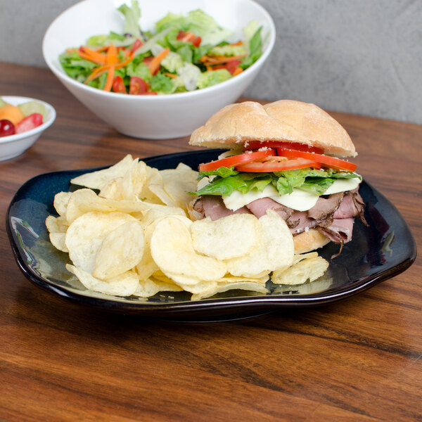 A Tuxton Artisan china pasta plate with a sandwich and chips on a table.