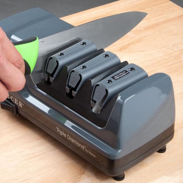 A Mercer Culinary knife being sharpened in a black electric knife sharpener.