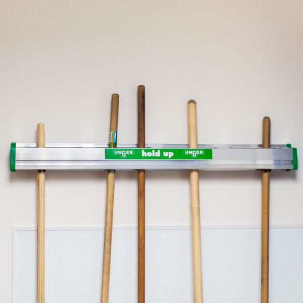 A Unger Hold Up Tool Holder with three poles holding brooms.