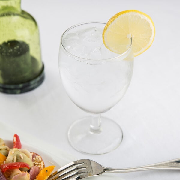 An Arcoroc Balloon goblet filled with ice and a lemon slice next to a plate of food