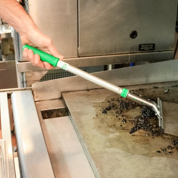 A hand holding a Unger GSH40 high heat griddle squeegee with a green handle.