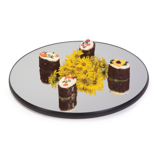 A Geneva round mirror food display tray with desserts and flowers on it.