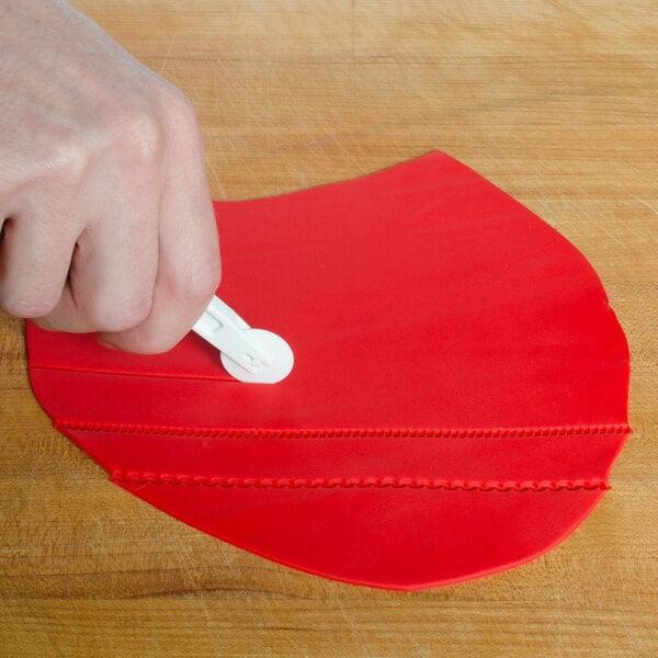 A hand using an Ateco fondant cutter with a red heart wheel.