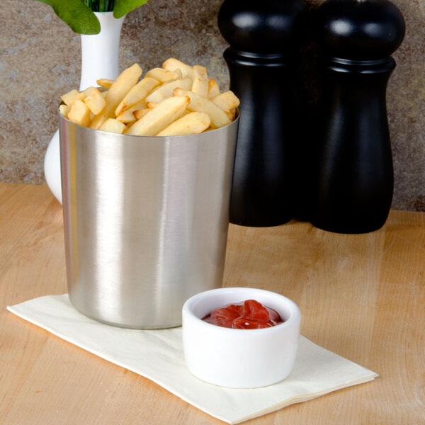 A silver American Metalcraft stainless steel cup filled with french fries on a table with a bowl of ketchup.