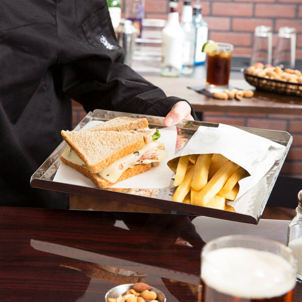 A person holding an American Metalcraft stainless steel tray of sandwiches and fries.