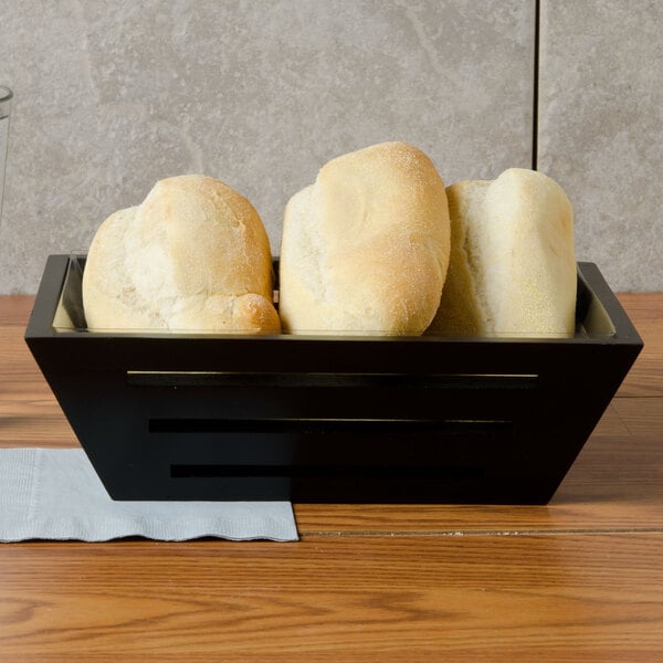 A black rectangular bread basket filled with bread on a table.