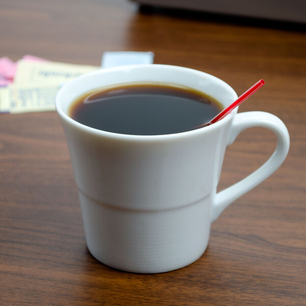 An Arcoroc coffee cup filled with coffee and a red straw.