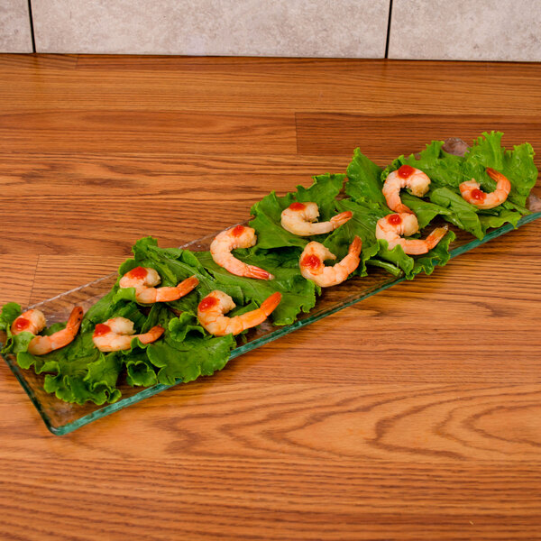 A rectangular clear glass platter of shrimp on a wood table.