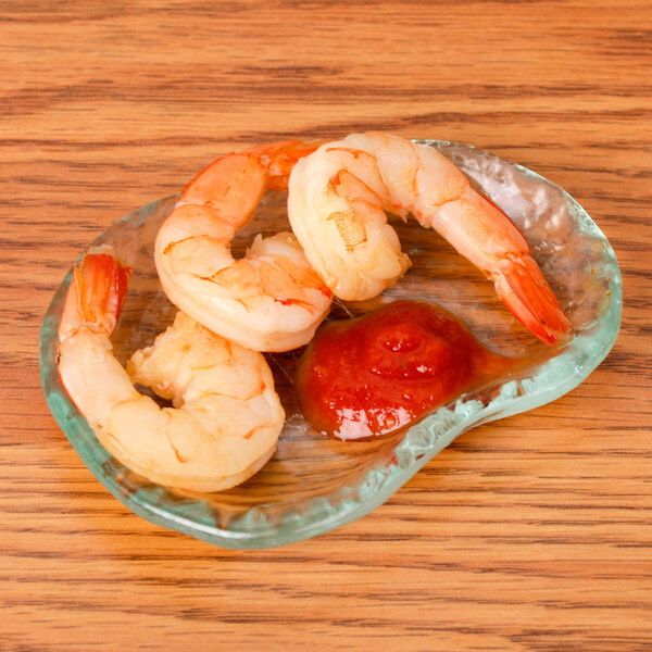 A shrimp on a 10 Strawberry Street Ocean Clear glass elliptical dish with sauce.