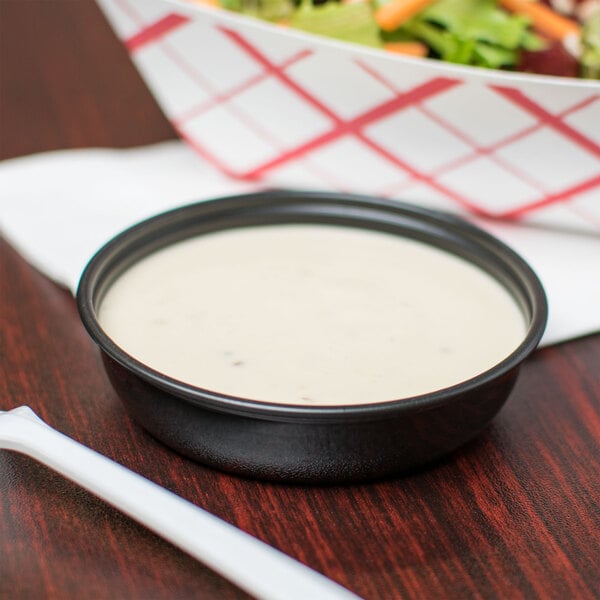 A bowl of salad with Solo black sauce cups of white sauce on the side.