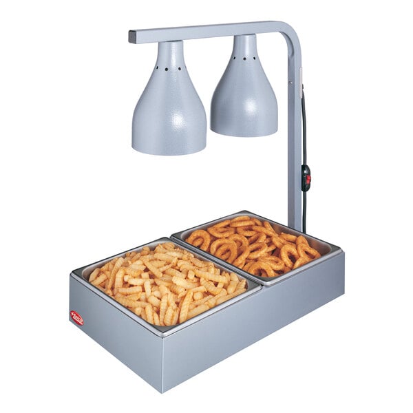 A Hatco white countertop lamp warmer with two bulbs heating a container of french fries.