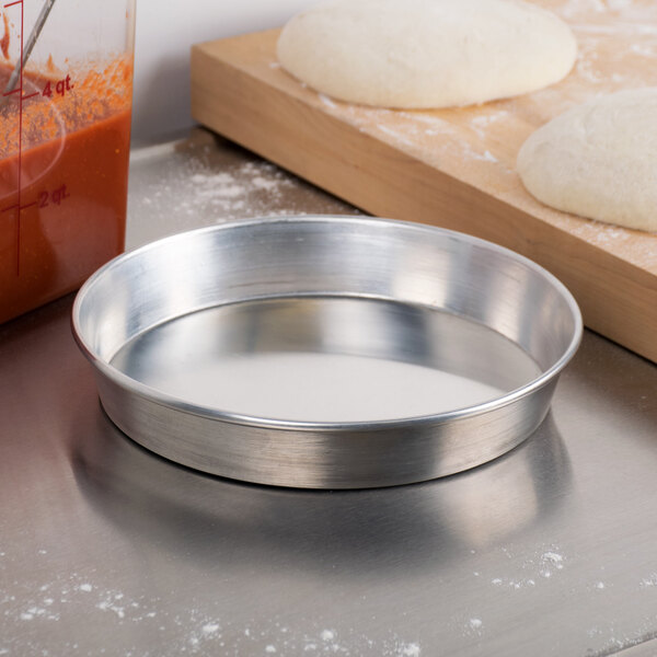 An American Metalcraft heavy weight aluminum pizza pan with dough on a floured counter.