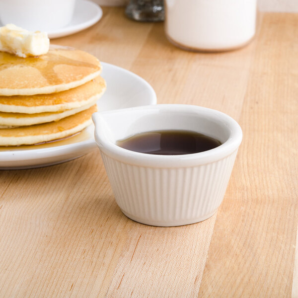 A stack of pancakes with butter on top and a Tuxton fluted white ramekin filled with syrup.