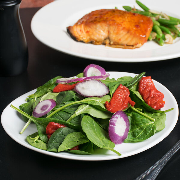 A 10 Strawberry Street white porcelain oval plate with salad and salmon on a table.