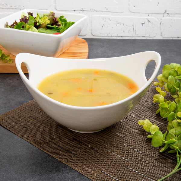 A Whittier white porcelain bowl with cut outs holding a bowl of soup and salad on a table.