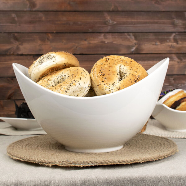 A white porcelain bowl with cut outs filled with bagels.